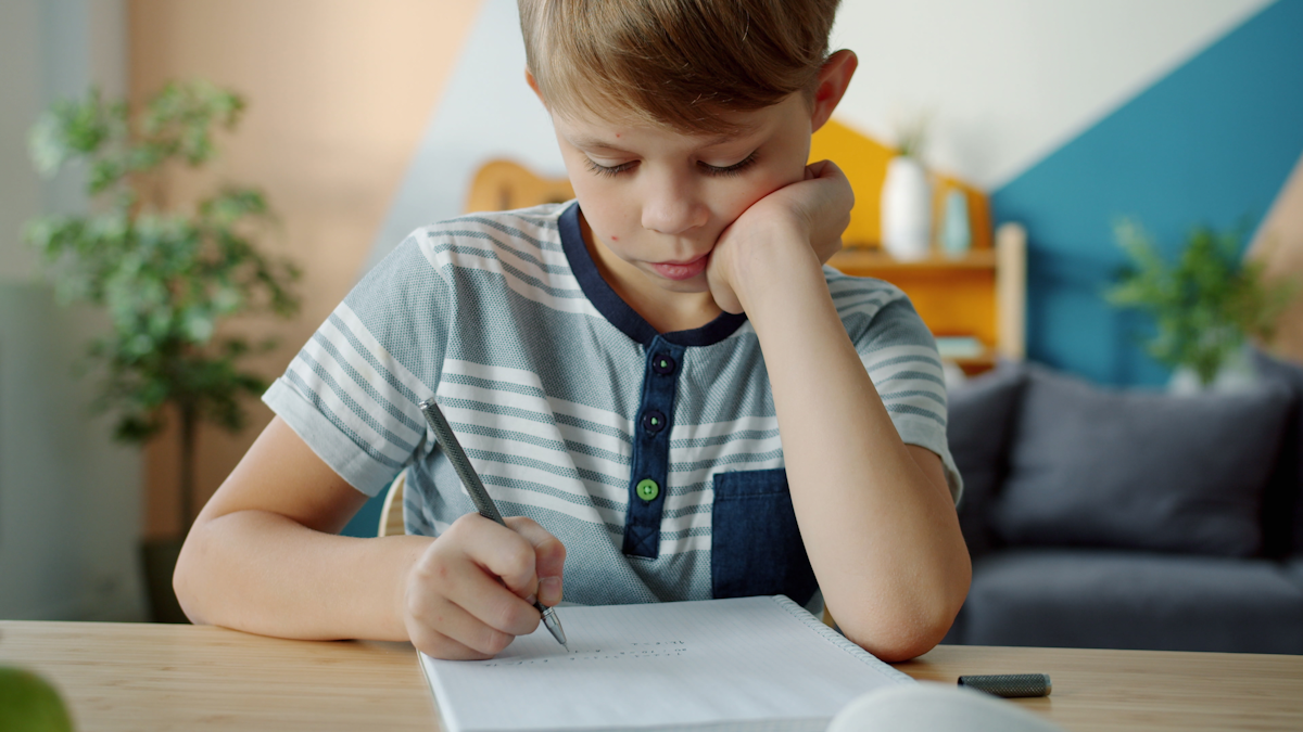 Menino concentrado fazendo lição em mesa com caderno e lápis